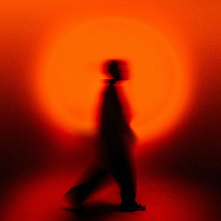 Figura in controluce che cammina dentro un bagliore arancione